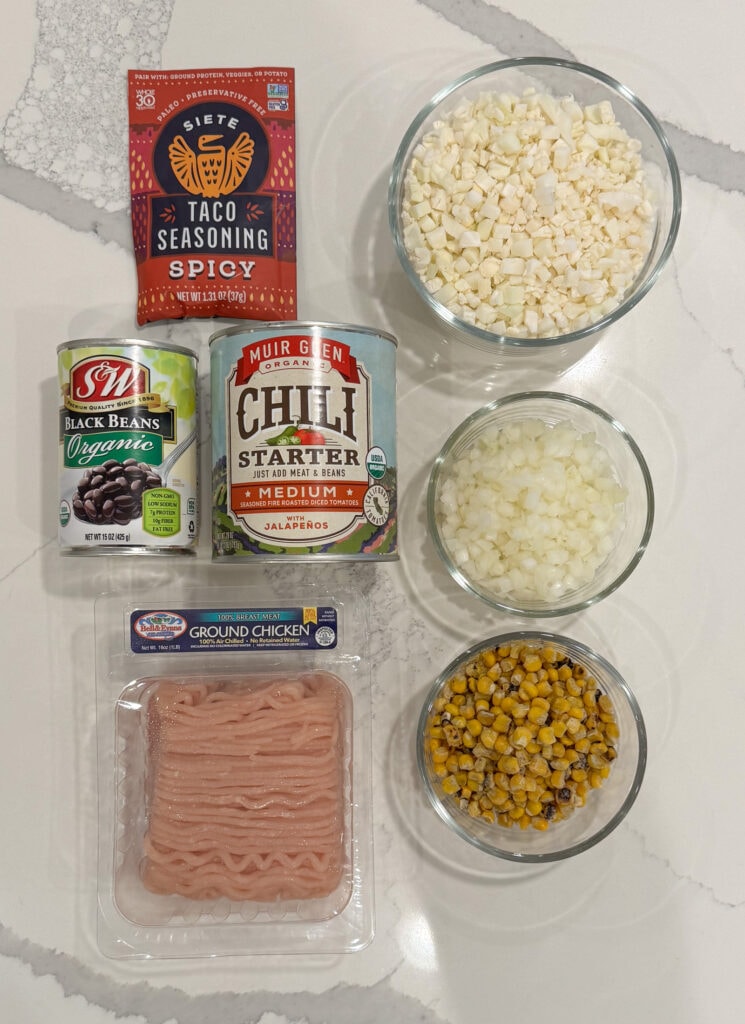 taco seasoning, riced cauliflower, black beans in a can, frozen roasted corn, fire roasted crushed tomatoes in a can, diced white onion, and ground chicken breast