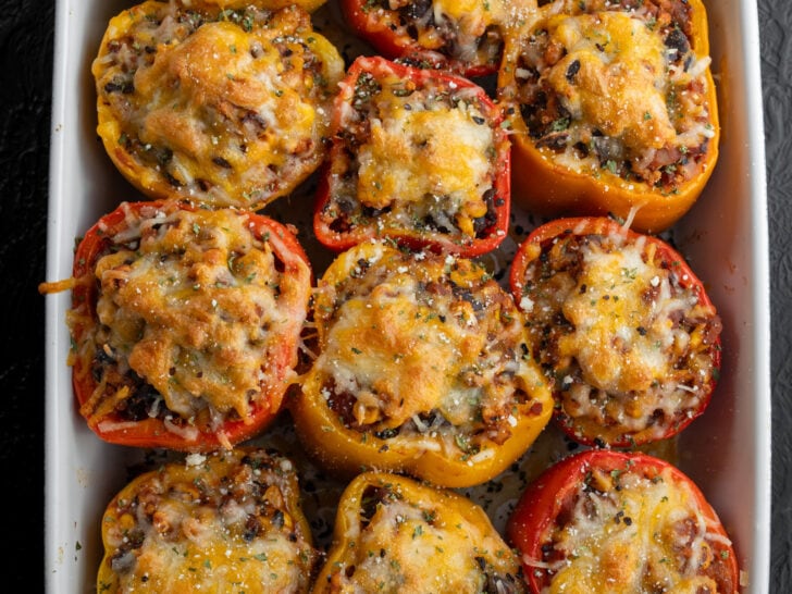 12 ground chicken stuffed peppers in a baking dish garnished with herbs, cotija cheese, and chile flakes