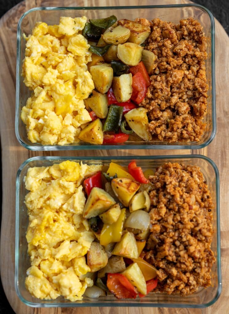 two glass meal prep bowls with scrambled eggs, chipotle pineapple ground chicken, and roasted veggies