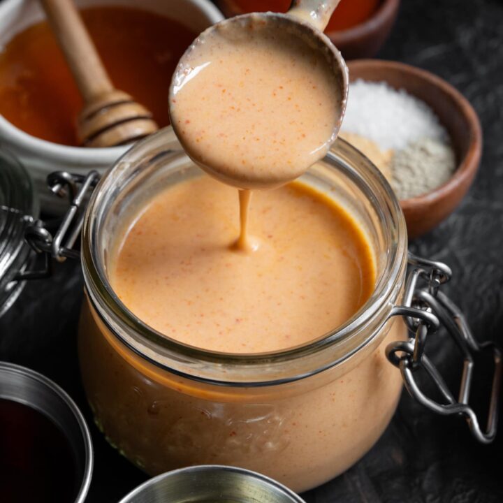 low calorie yum yum sauce in a glass jar with a wooden spoon dipped inside