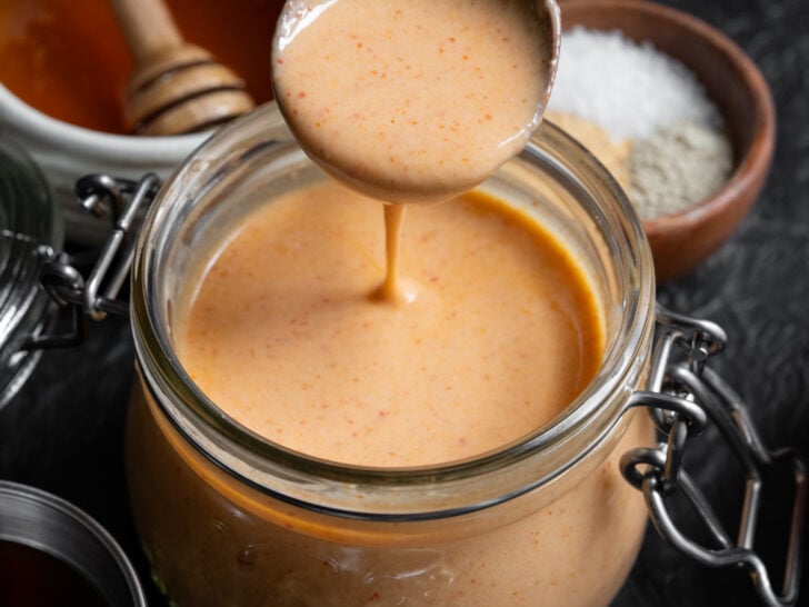 low calorie yum yum sauce in a glass jar with a wooden spoon dipped inside
