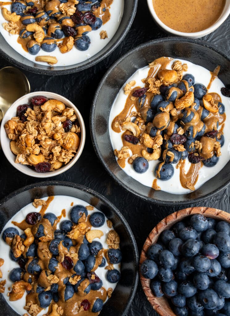 3 breakfast bowls with Greek yogurt, fresh blueberries, almond butter, and homemade granola