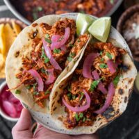 two rotisserie chicken tacos with lime wedges, cilantro, and pickled onions