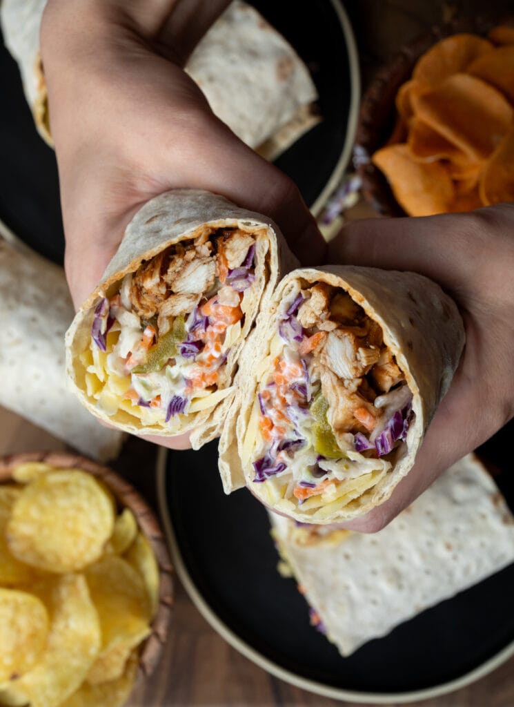 holding a flatbread wrap with rotisserie chicken, cabbage slaw, pickles, and cheddar cheese