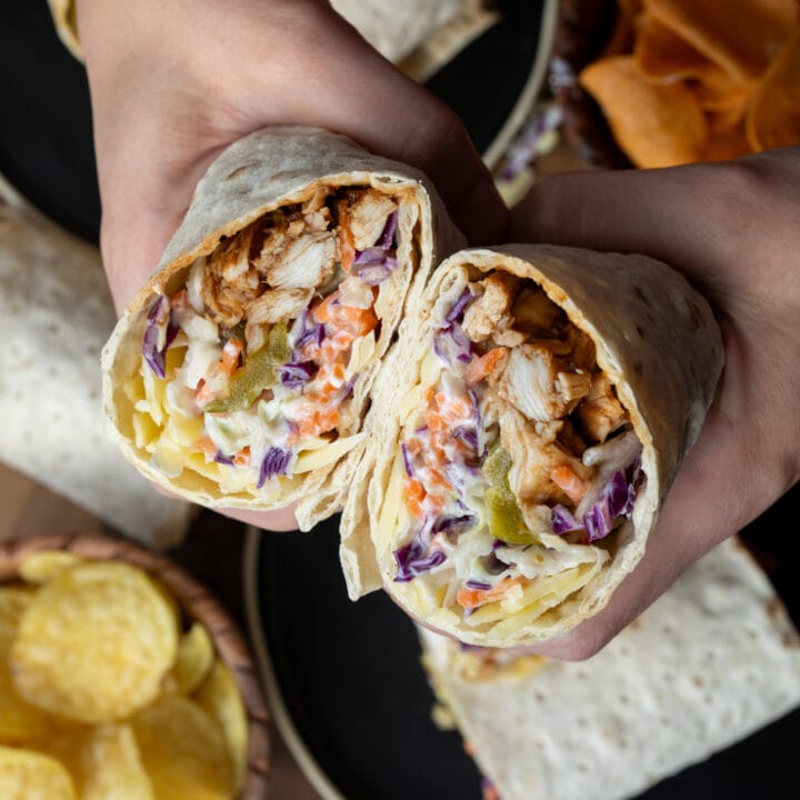 holding a rotisserie chicken wrap with cabbage slaw, pickled, and cheddar cheese