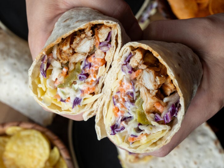 holding a rotisserie chicken wrap with cabbage slaw, pickled, and cheddar cheese