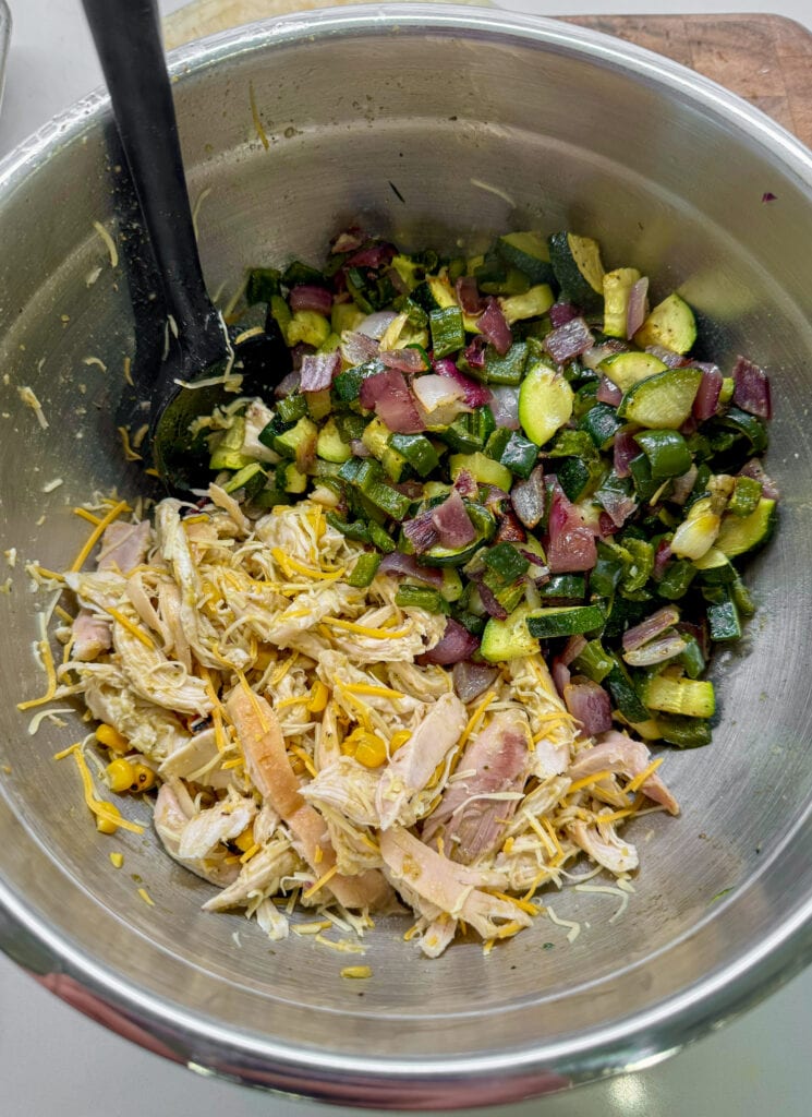 roasted zucchini, peppers, and onion in a mixing bowl with pulled rotisserie chicken, frozen corn, and shredded cheese