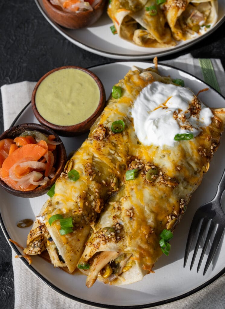 two rotisserie chicken enchiladas on a plate with small bowls of escabeche and jalapeño dip