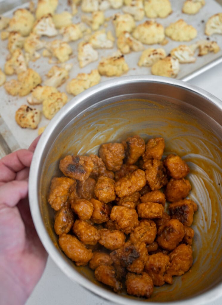 baked chicken breast chunks tossed in buffalo sauce inside a stainless steel mixing bowl