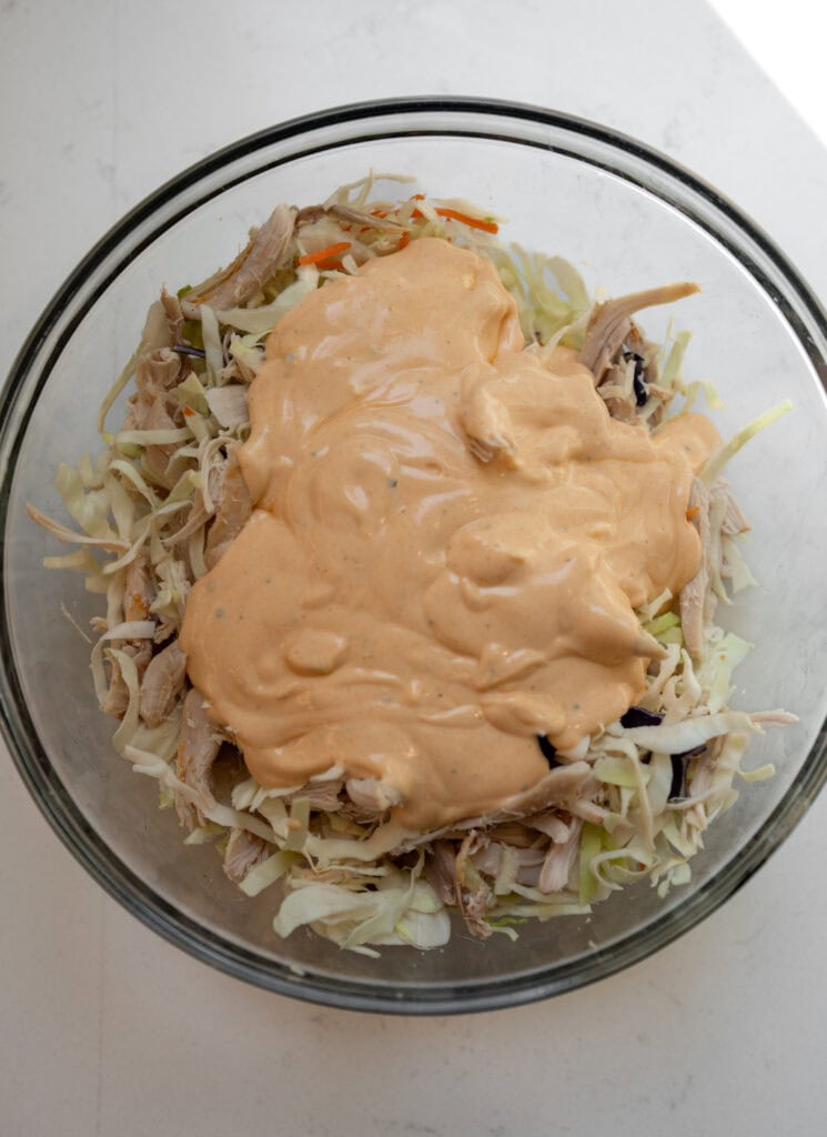 mixed chicken and coleslaw in a glass bowl with a blend of Greek yogurt, buffalo sauce, and ranch seasoning