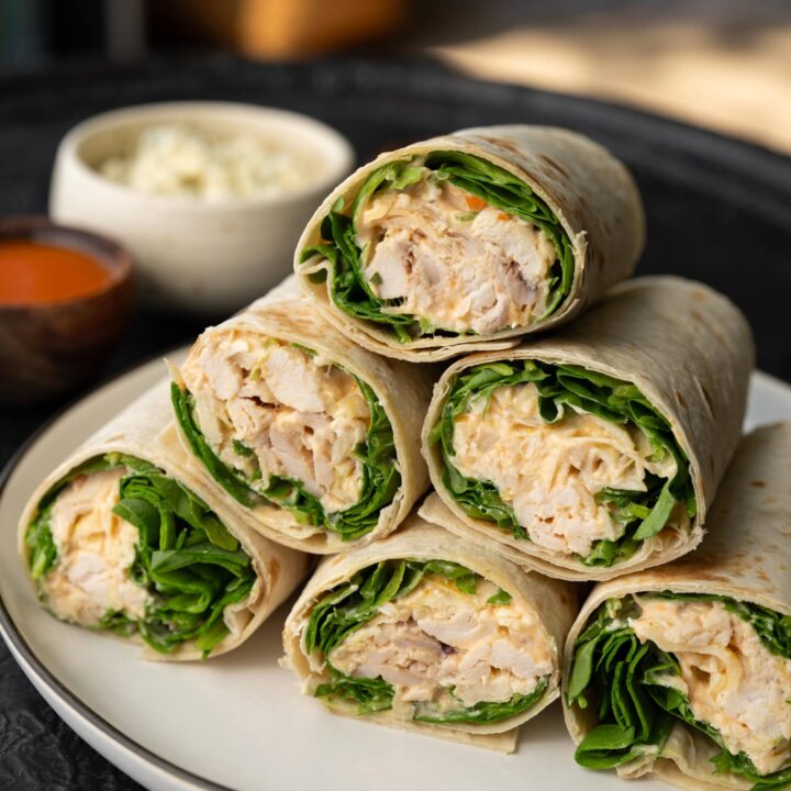 healthy buffalo chicken wraps stacked on a plate with buffalo sauce and blue cheese crumbles