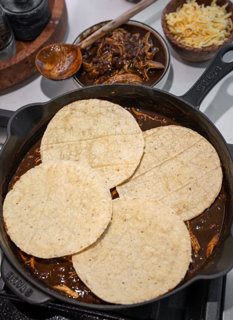 four corn tortillas in a skillet with chicken mole and black beans