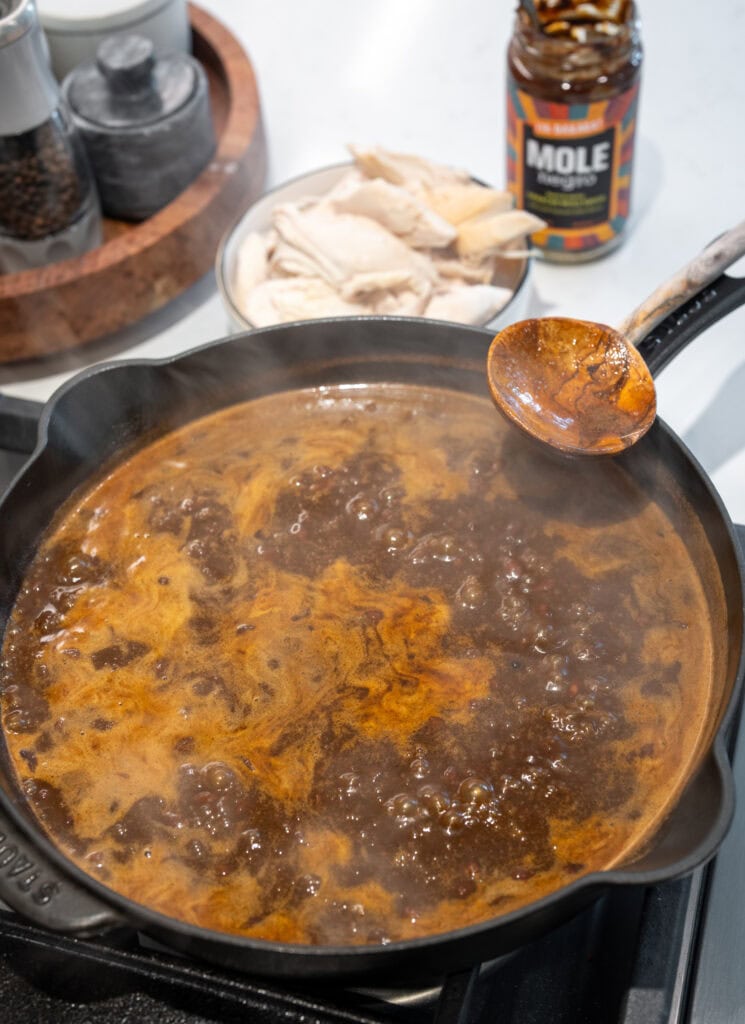 cooking down mole negro sauce, chicken bone broth, and black beans in a cast iron skillet