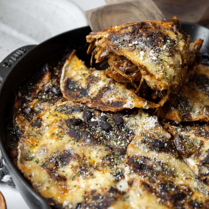 serving a slice of chicken mole enchilada casserole out of a cast iron skillet with a wooden spatula