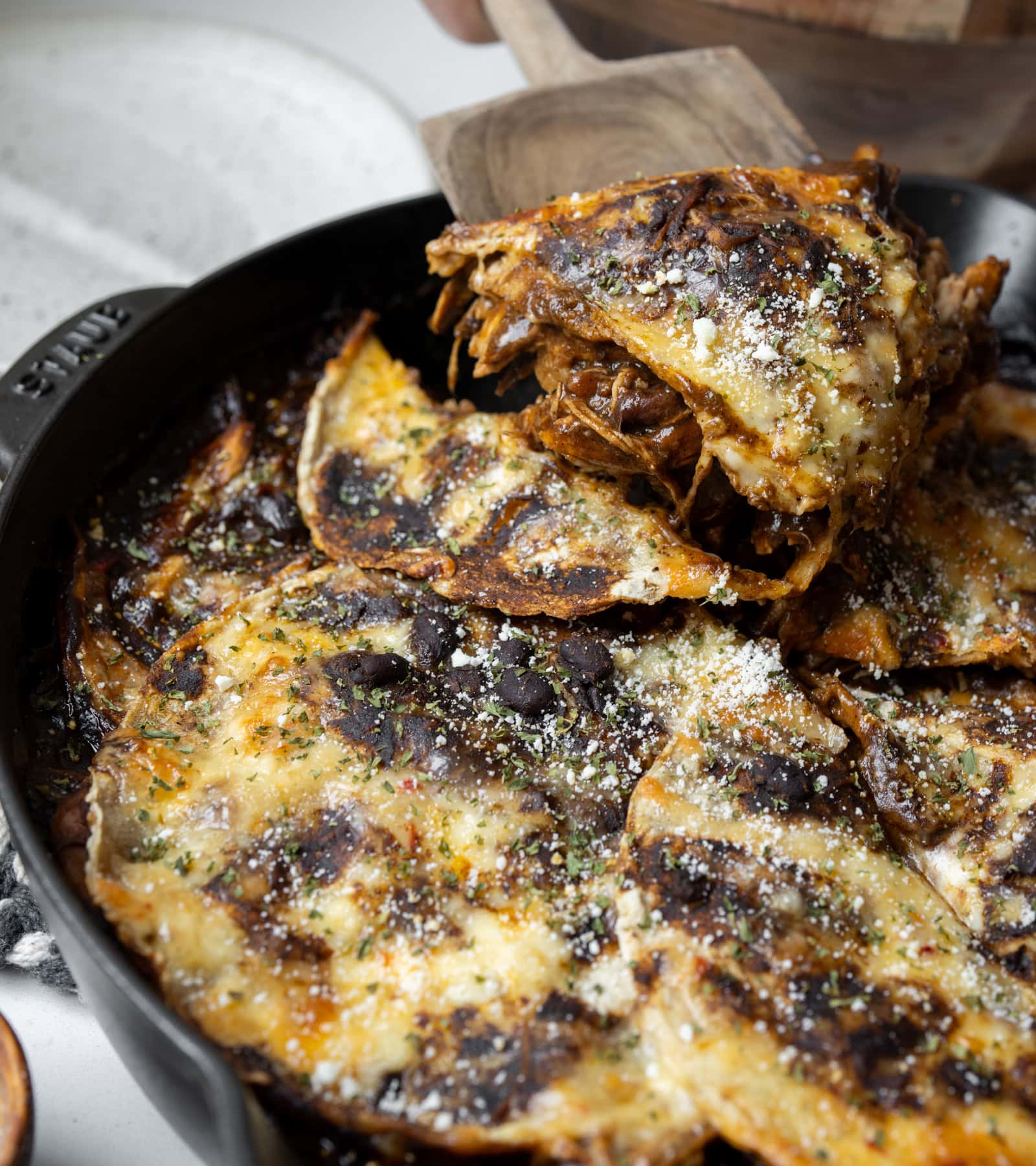 serving a slice of chicken mole enchilada casserole out of a cast iron skillet with a wooden spatula