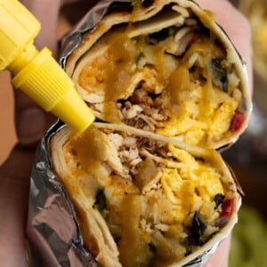 drizzling hot sauce over the cross section of a chicken breakfast burrito