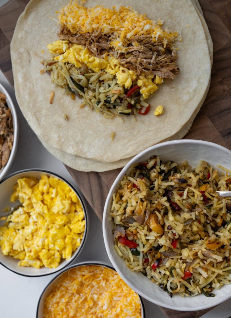 filling flour tortillas with roasted hash browns and fajita vegetables, Mexican seasoned rotisserie chicken, scrambled eggs, and colby jack cheese