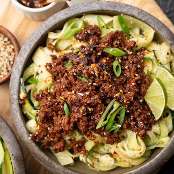 zucchini noodles in a bowl topped with chili crunch ground bison, sesame garlic crunch, and sliced scallions