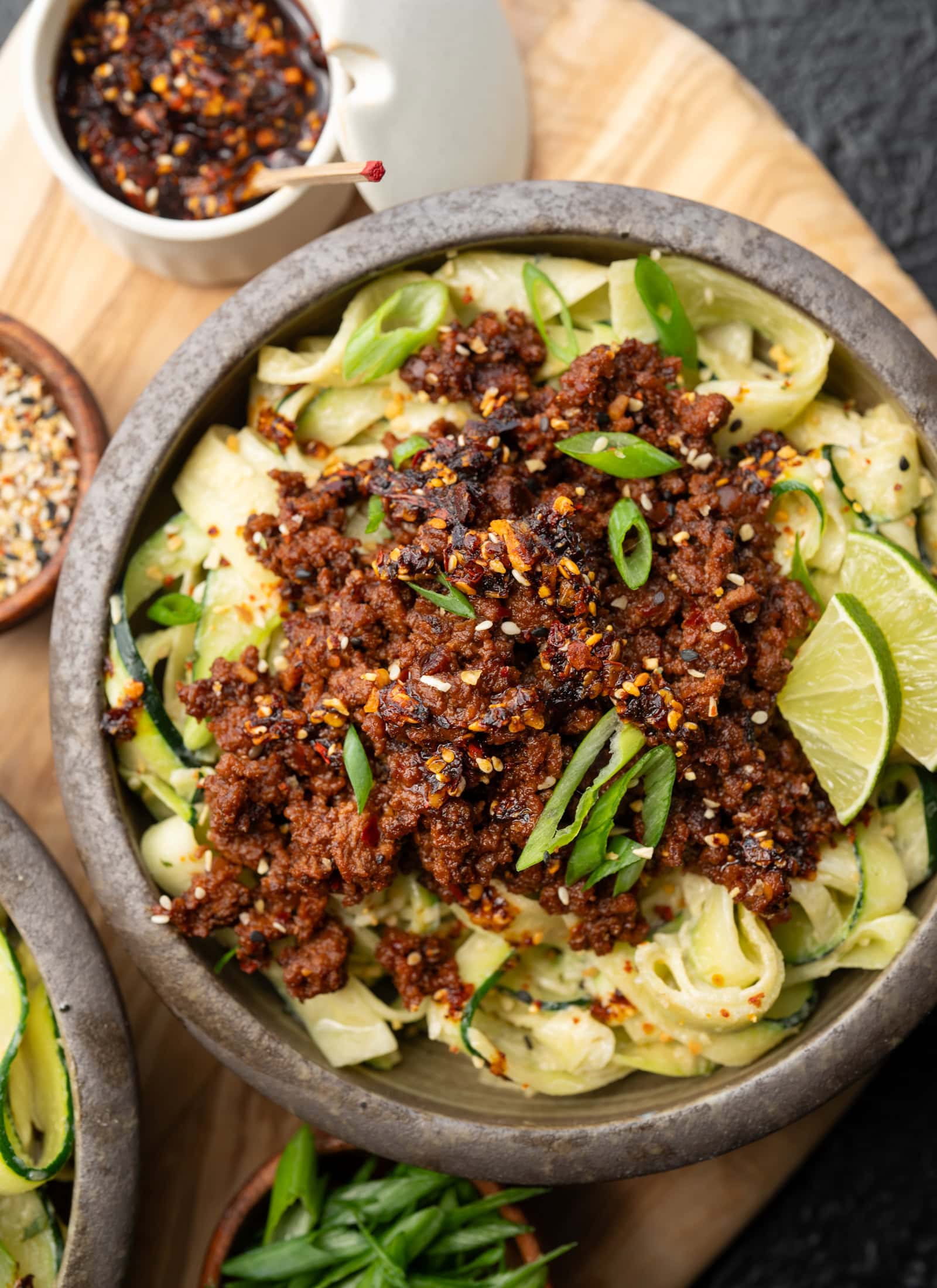 zucchini noodles in a bowl topped with chili crunch ground bison, sesame garlic crunch, and sliced scallions