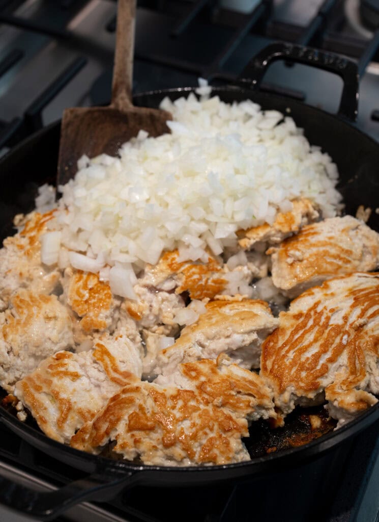 browning ground chicken in a cast iron braising pan with diced sweet onion