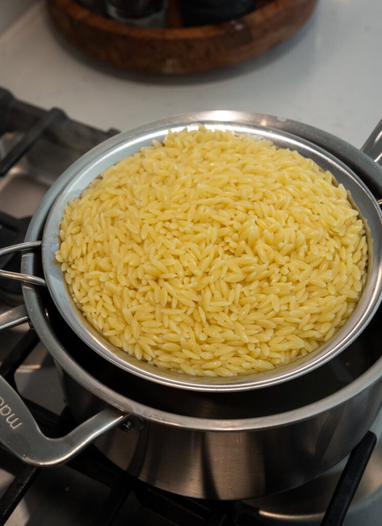 cooked orzo in a mesh strainer over a stainless steel pot