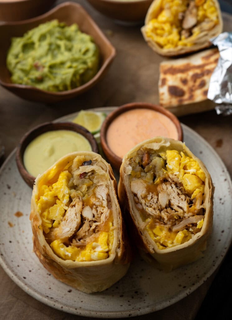 chicken breakfast burrito cut in half on a plate with two salsas and lime wedges
