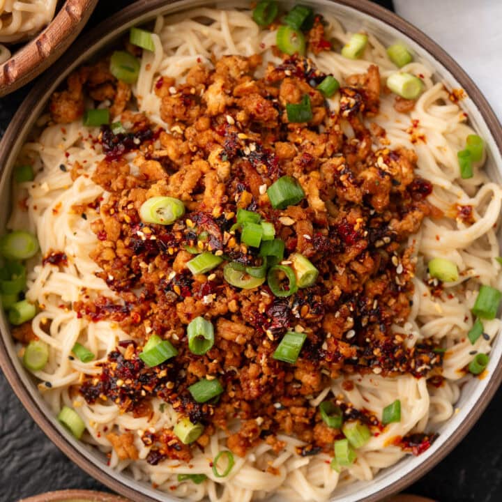 chili crisp ground chicken over peanut butter rice ramen noodles in a bowl garnished with green onions, sesame seeds, and chili oil
