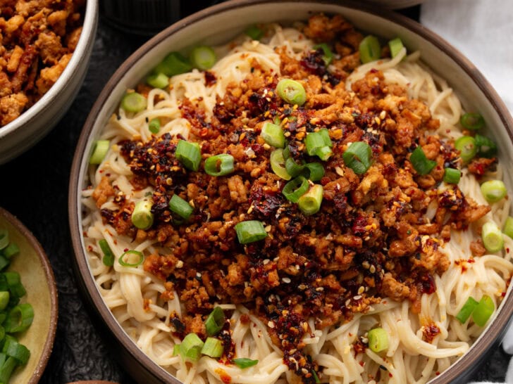 peanut butter noodle bowls topped with chili crisp ground chicken, toasted sesame seeds, and sliced scallions