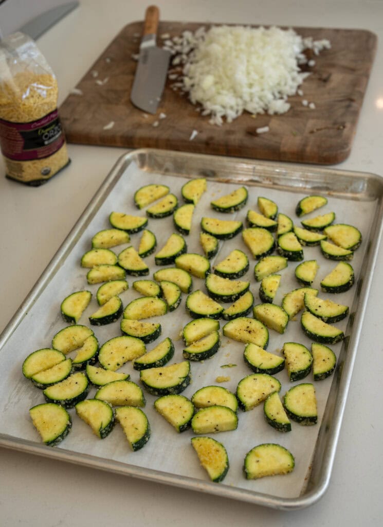 zucchini half moons on a sheet pan tossed in olive oil, grated parmesan, and garlic powder