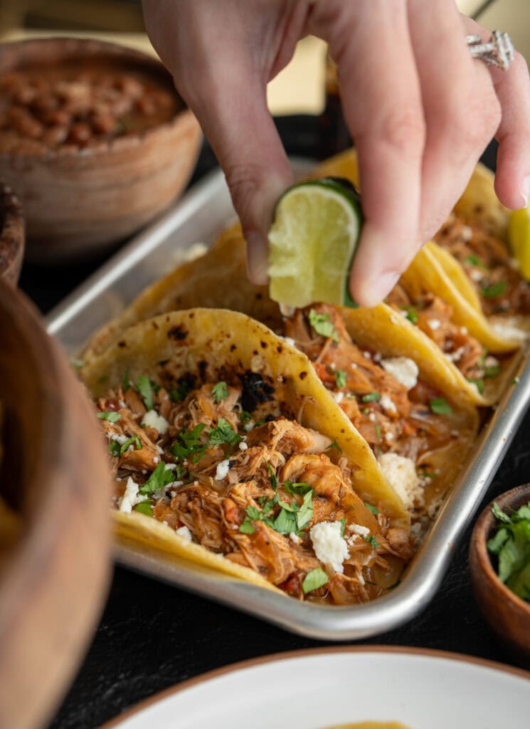 squeezing a lime wedge over a slow cooked chicken taco