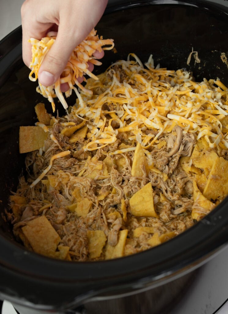 topping a mixture of shredded chicken and corn tortilla strips with shredded colby jack cheese