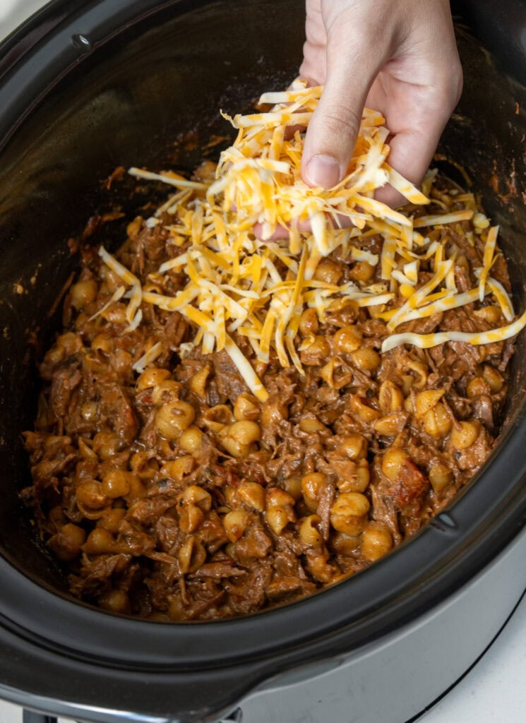 sprinkling shredded colby jack cheese over chili mac in a slow cooker