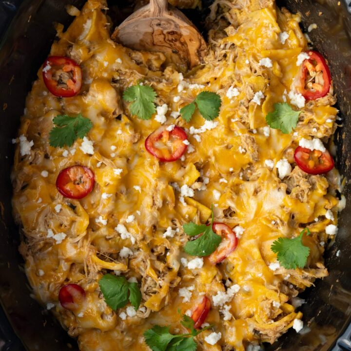 chicken enchilada casserole in a Crockpot with a wooden serving spoon