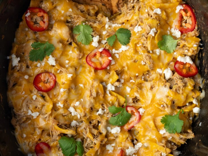 chicken enchilada casserole in a Crockpot with a wooden serving spoon