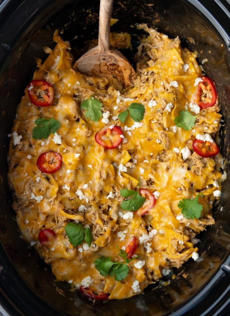 chicken enchilada casserole in a Crockpot with a wooden serving spoon