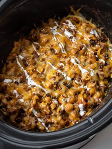 pulled beef chili mac and cheese in a Crockpot garnished with Mexican crema and salsa macha