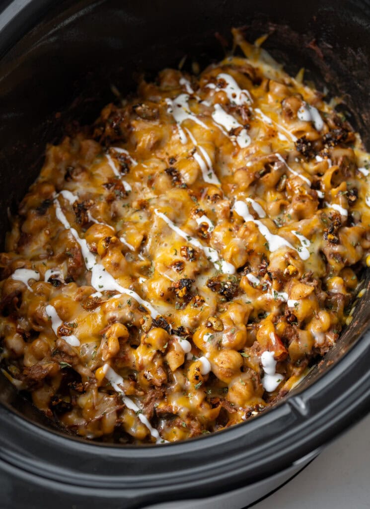 pulled beef chili mac and cheese in a Crockpot garnished with Mexican crema and salsa macha