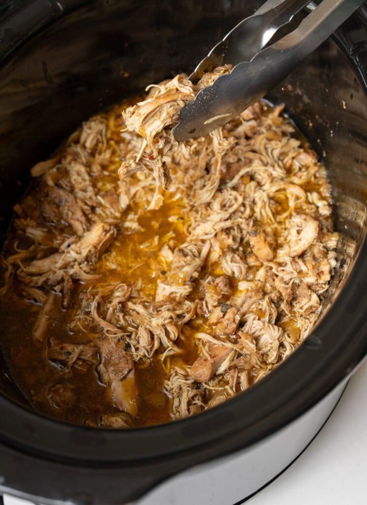 using tongs to serve Mexican shredded chicken from a Crockpot