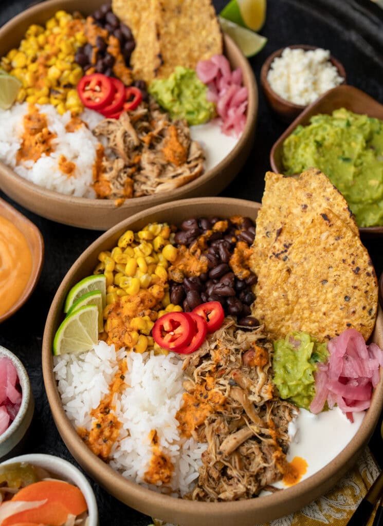 two slow cooked chicken burrito bowls with garnishes