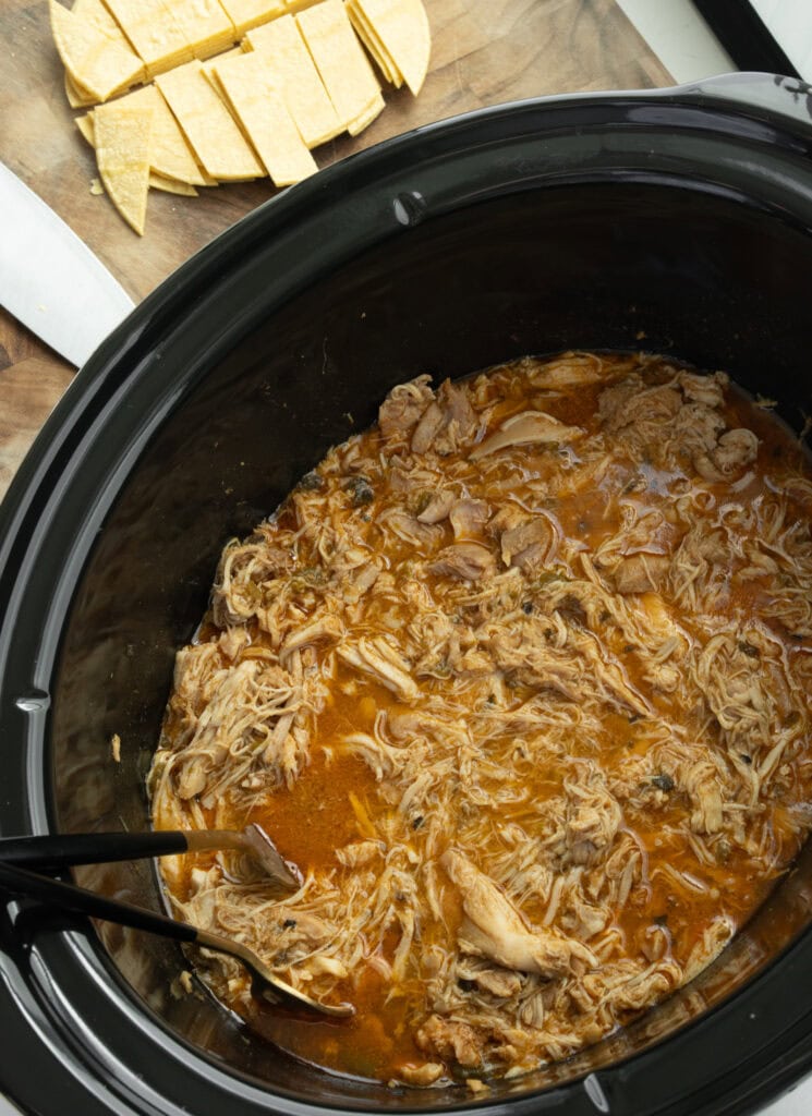 shredded chicken in a Crockpot with corn tortillas cut into strips on a cutting board