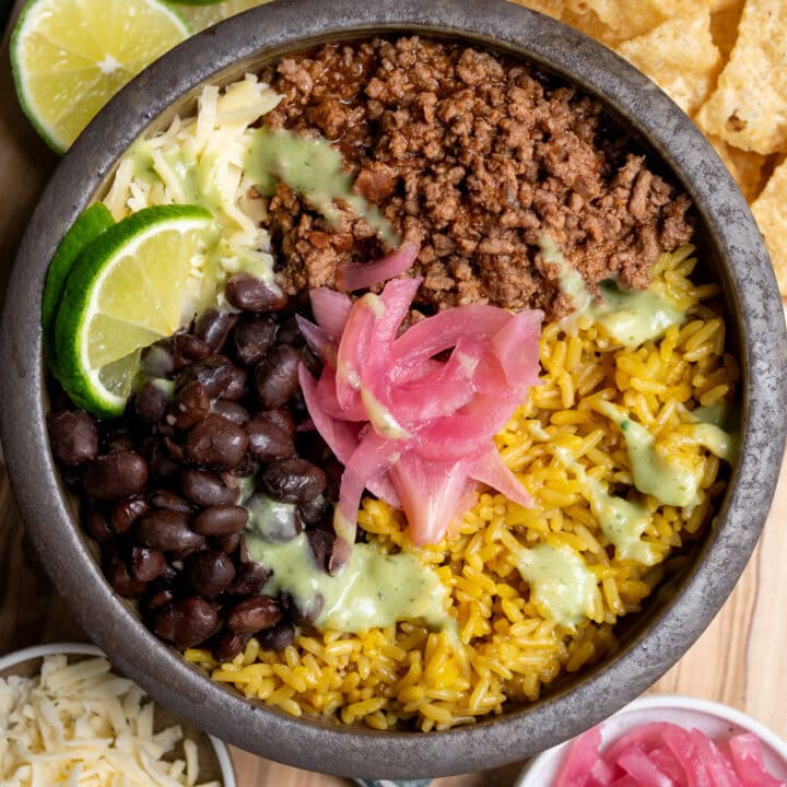 ground beef birria burrito bowl with rice, black beans, cheese, pickled onions, lime wedges, and salsa verde