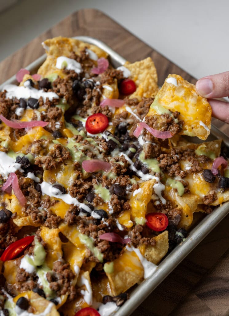 picking up a nacho from a sheet pan of ground beef birria nachos