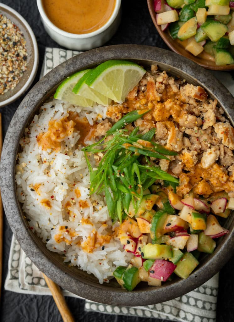 rice bowl with sesame ginger ground chicken, cucumber and radish crunch salad, scallions, toasted sesame seeds, and lime wedges