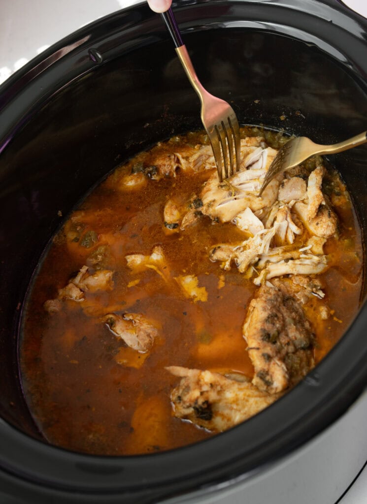 shredding slow cooked chicken in a Crockpot with two forks