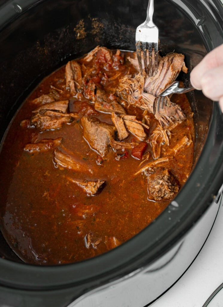 shredding top round roast in a slow cooker with two forks