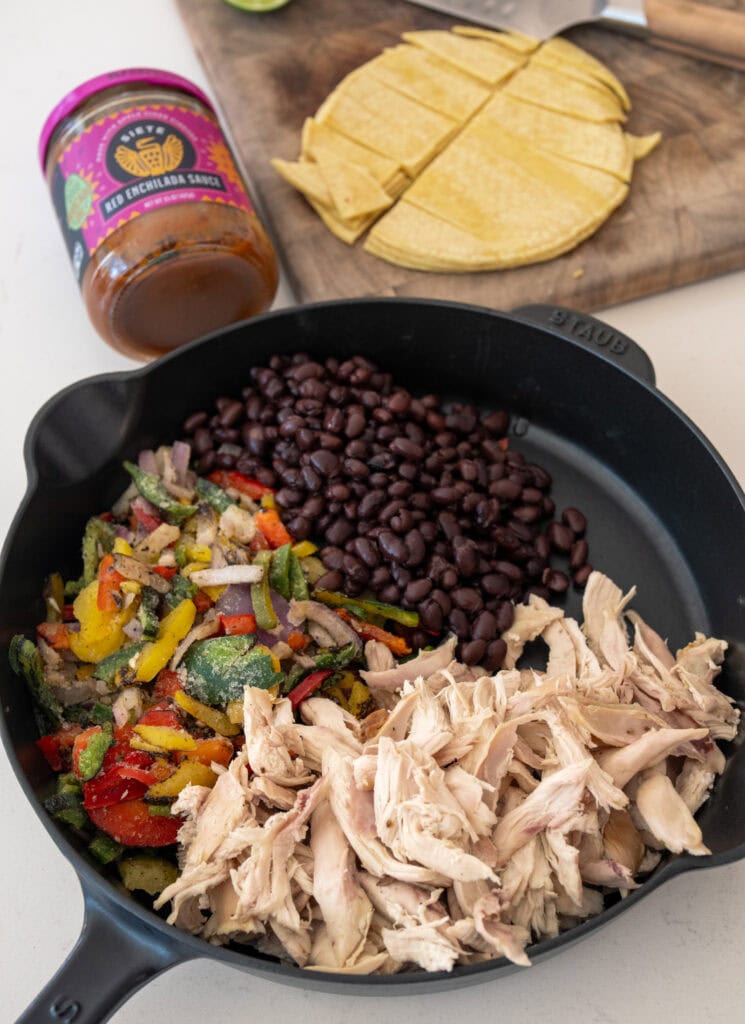 drained black beans, pulled rotisserie chicken, frozen fajita veggies, red enchilada sauce, and chopped corn tortillas in a cast iron skillet