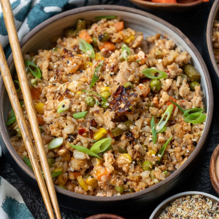 bowl of ground chicken fried rice garnished with sliced scallions, chili oil, yum yum sauce, and a side of pickled carrots