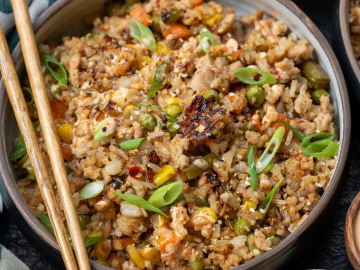 bowl of ground chicken fried rice garnished with sliced scallions, chili oil, yum yum sauce, and a side of pickled carrots