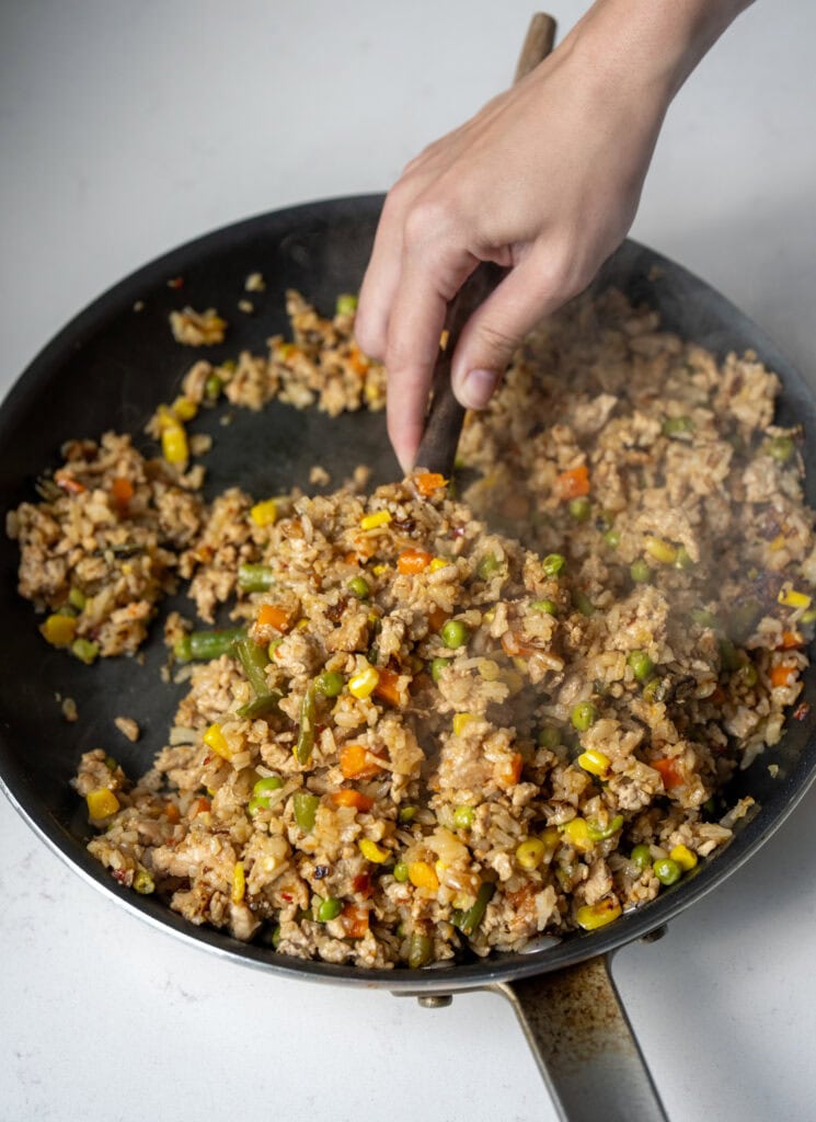 serving ground chicken fried rice out of a skillet with a wooden spatula