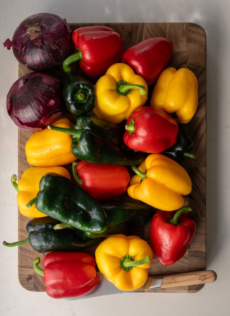 red and yellow bell peppers, poblano peppers, and red onions on a cutting board